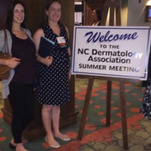 Three woman standing in front of summer meeting poster