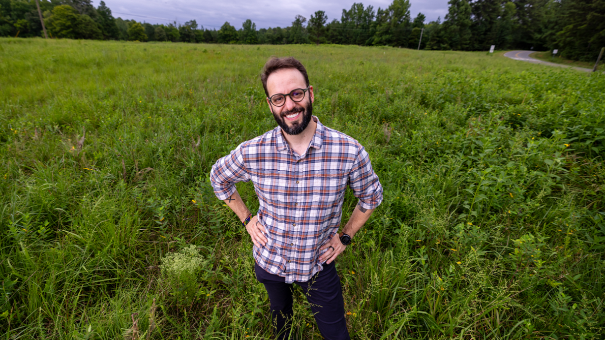 João Vissoci, PhD, an emergency medicine professor at Duke University School of Medicine, standing in a lush field with hands on hips