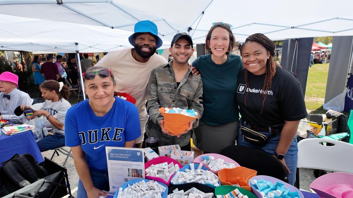 Five people from Duke Dermatology pose in front of their table at the Pride Vendor & Food Truck Rodeo.