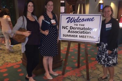 Three woman standing in front of summer meeting poster